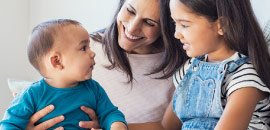 Mother with daughter and infant son sitting together and smiling. 