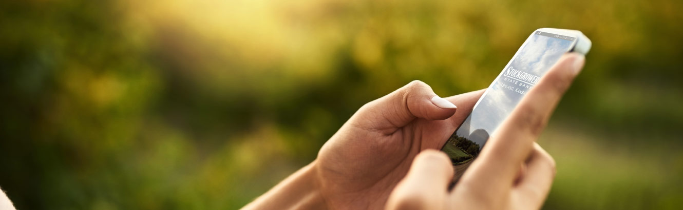 Person's hands holding a smartphone with the Stockgrowers Bank app on it.